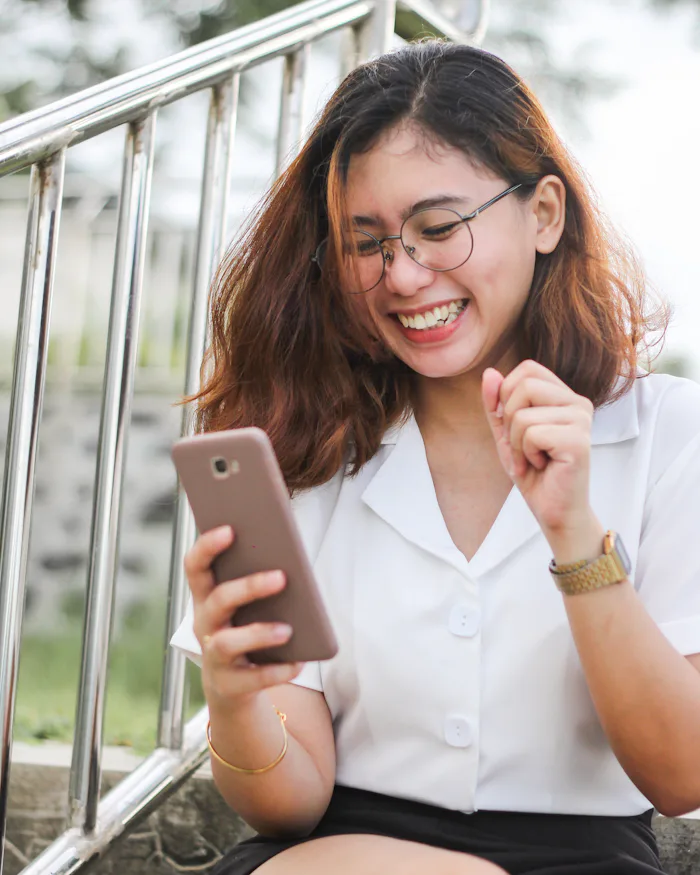 Woman in a white shirt smiling while looking at her smartphone
